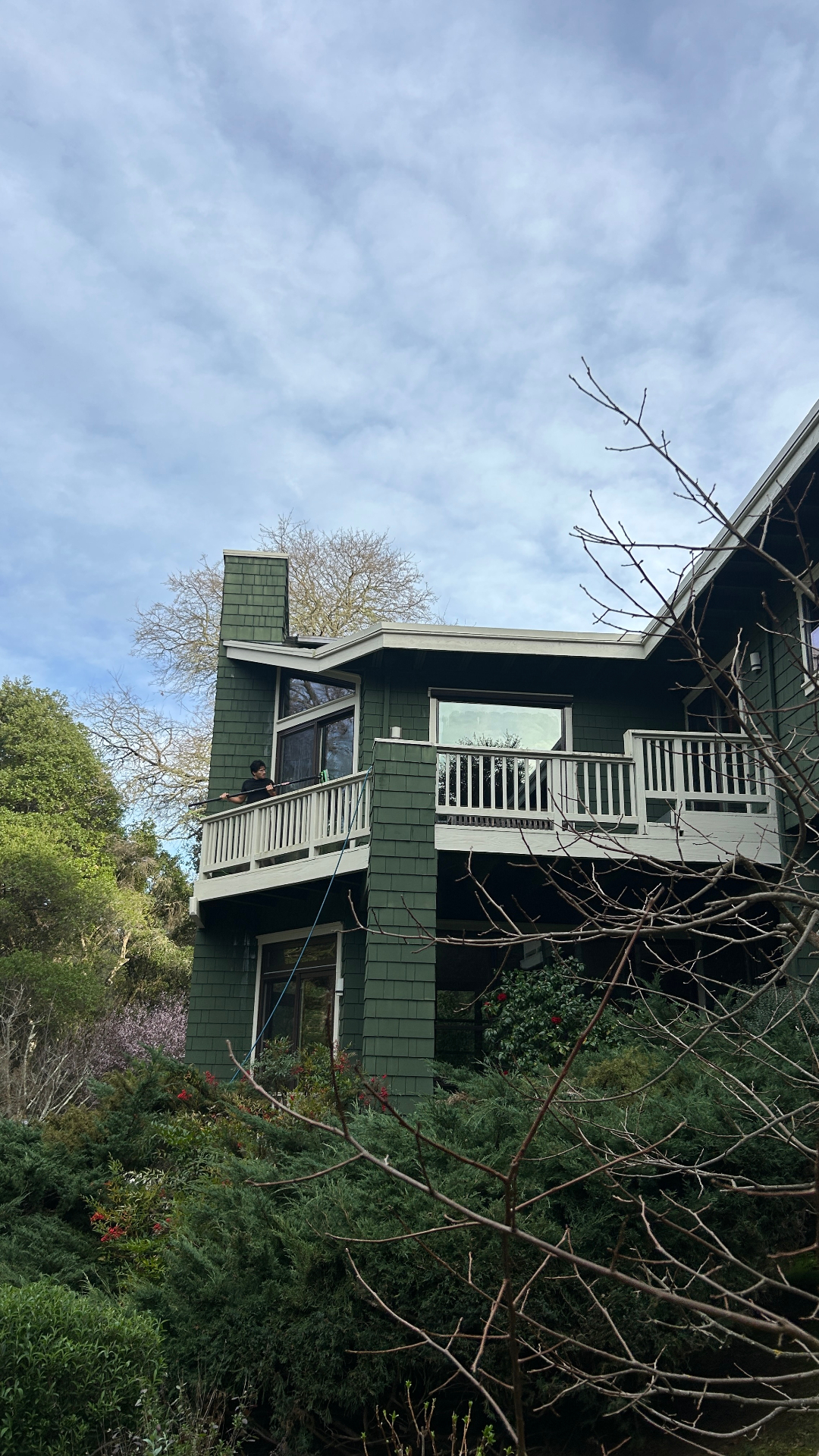 Technician cleaning upper-story windows on a green shingled home