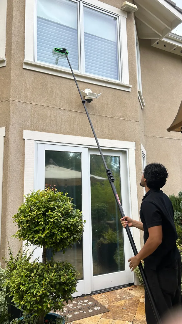 Technician cleaning second-story windows with a water-fed pole